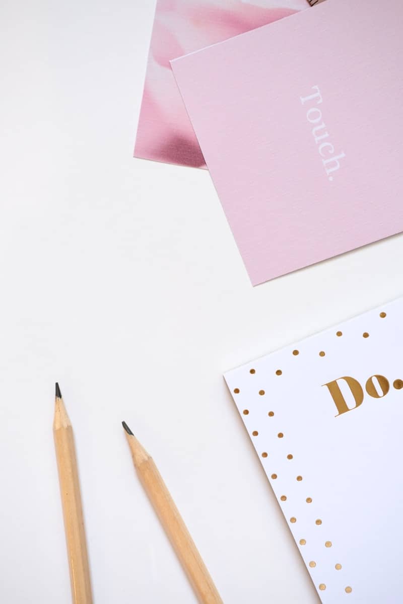 Two pencils and pink notebooks on white surface