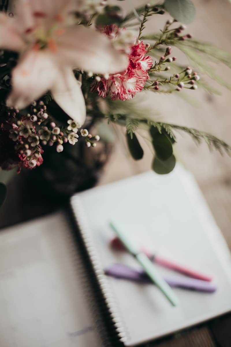 A notebook with a pen on top of it next to a bouquet of flowers