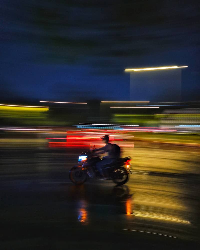 Motorcyclist speeds through a colorful, blurry night scene.