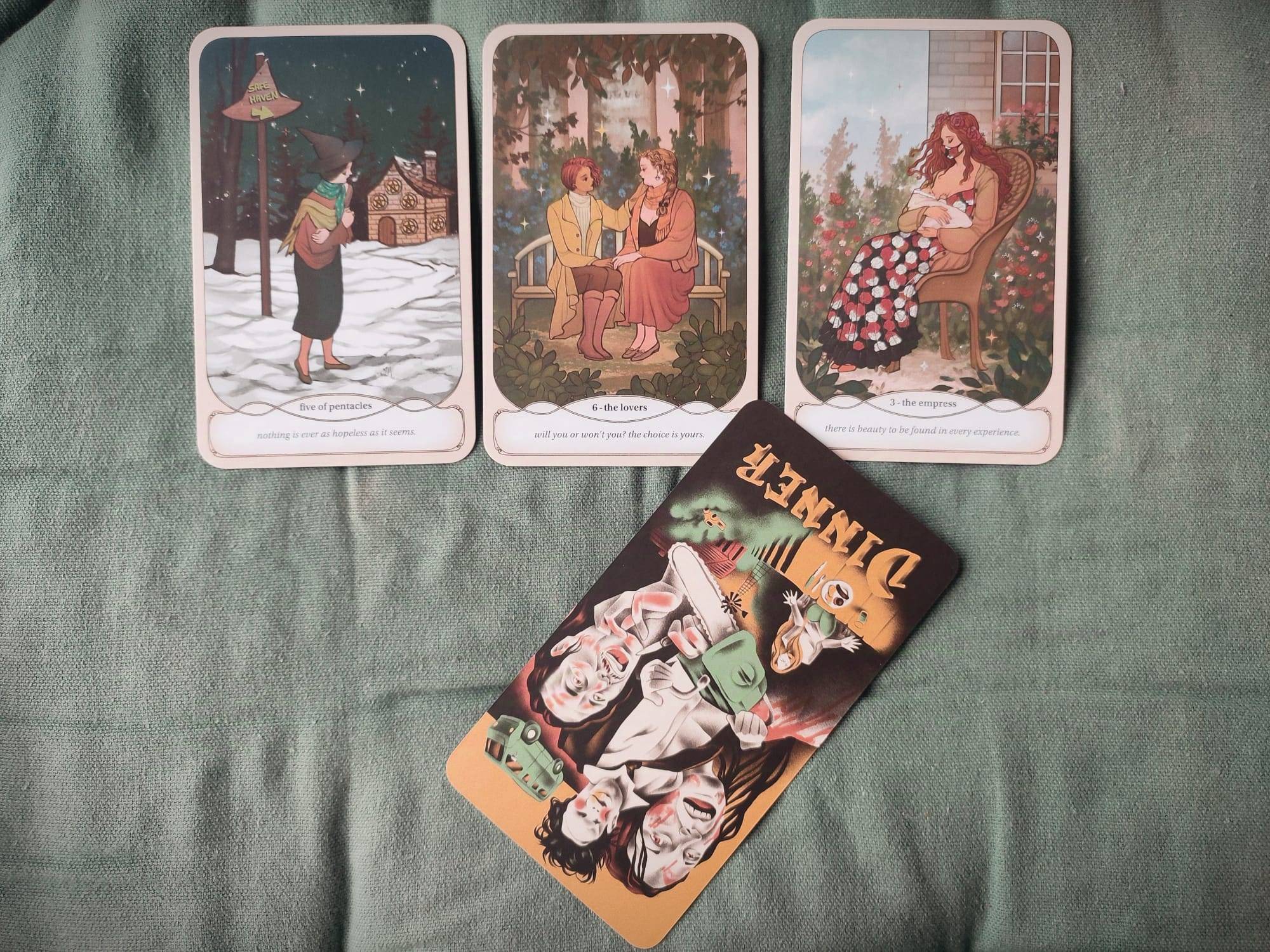 Tres cartas de tarot y una de oraculo sobre un cojin verde. Las cartas de tarot estan en fila, la del oraculo esta invertida debajo de la carta central.