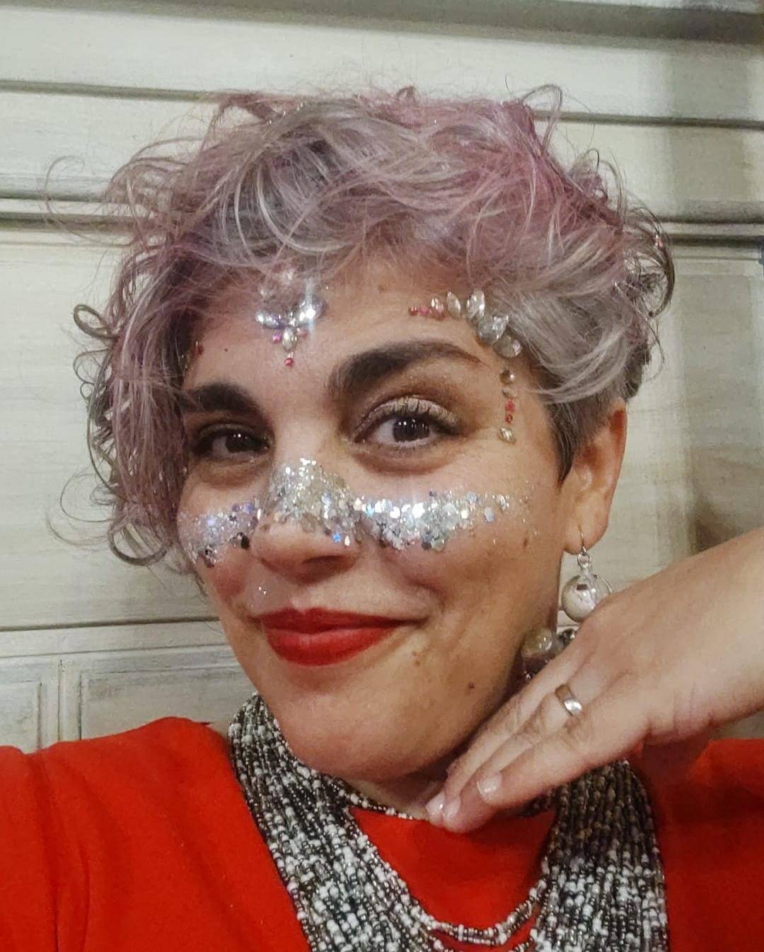 Mi cara llena de brillantina, pelo gris pintado de rosa, llevo un vestido rojo y unos pendientes de bola de navidad con un muñeco de nieve dentro y nieve que se mueve