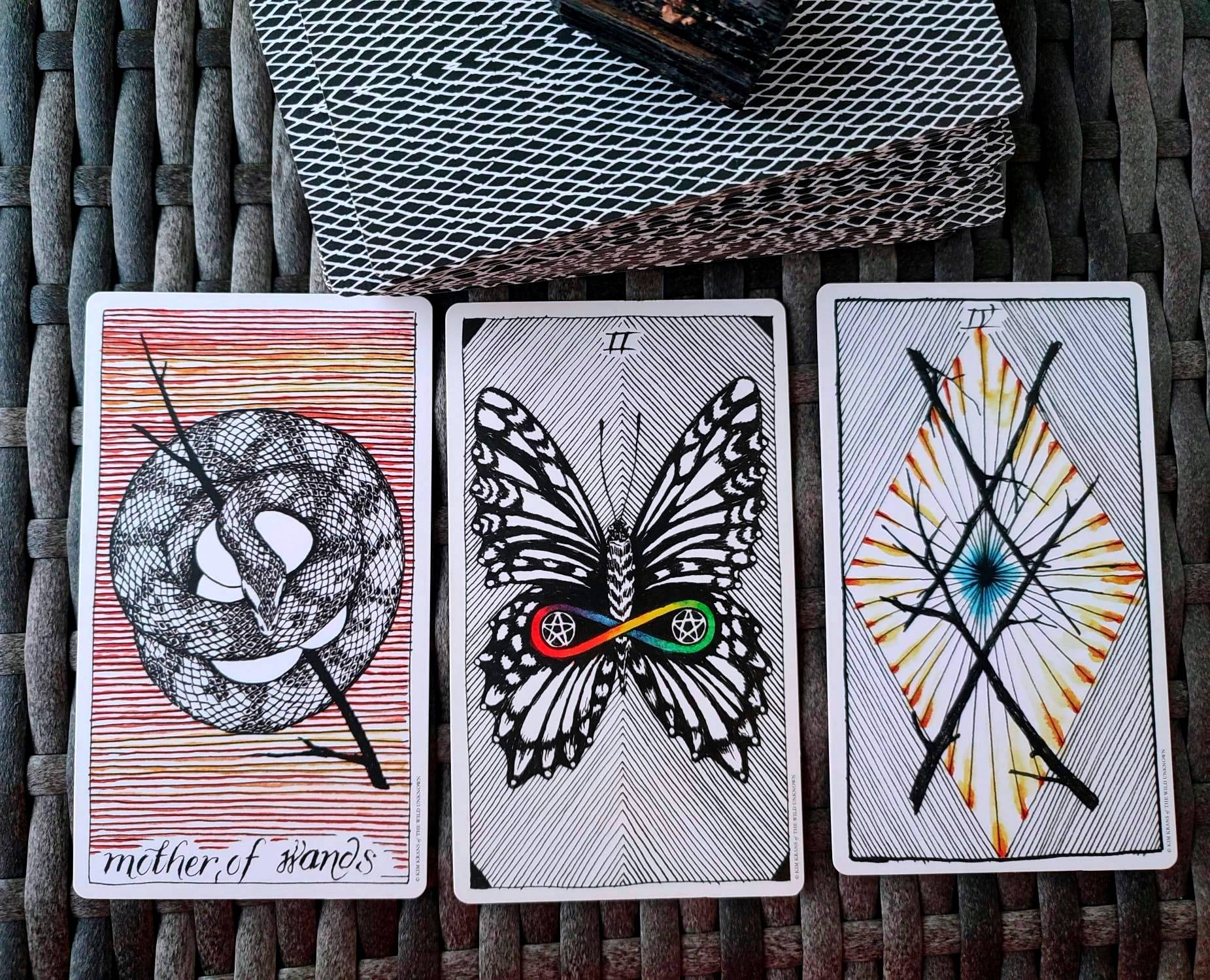 Tirada de 3 cartas de la baraja Wild Unknown: reina de bastos (una serpiente protegiendo sus huevos), 2 de oros (una mariposa con dos monedas, una en cada ala, y un signo de infinito de arco iris envolviendolas), y 4 de bastos (4 palos forman un rombo, y 