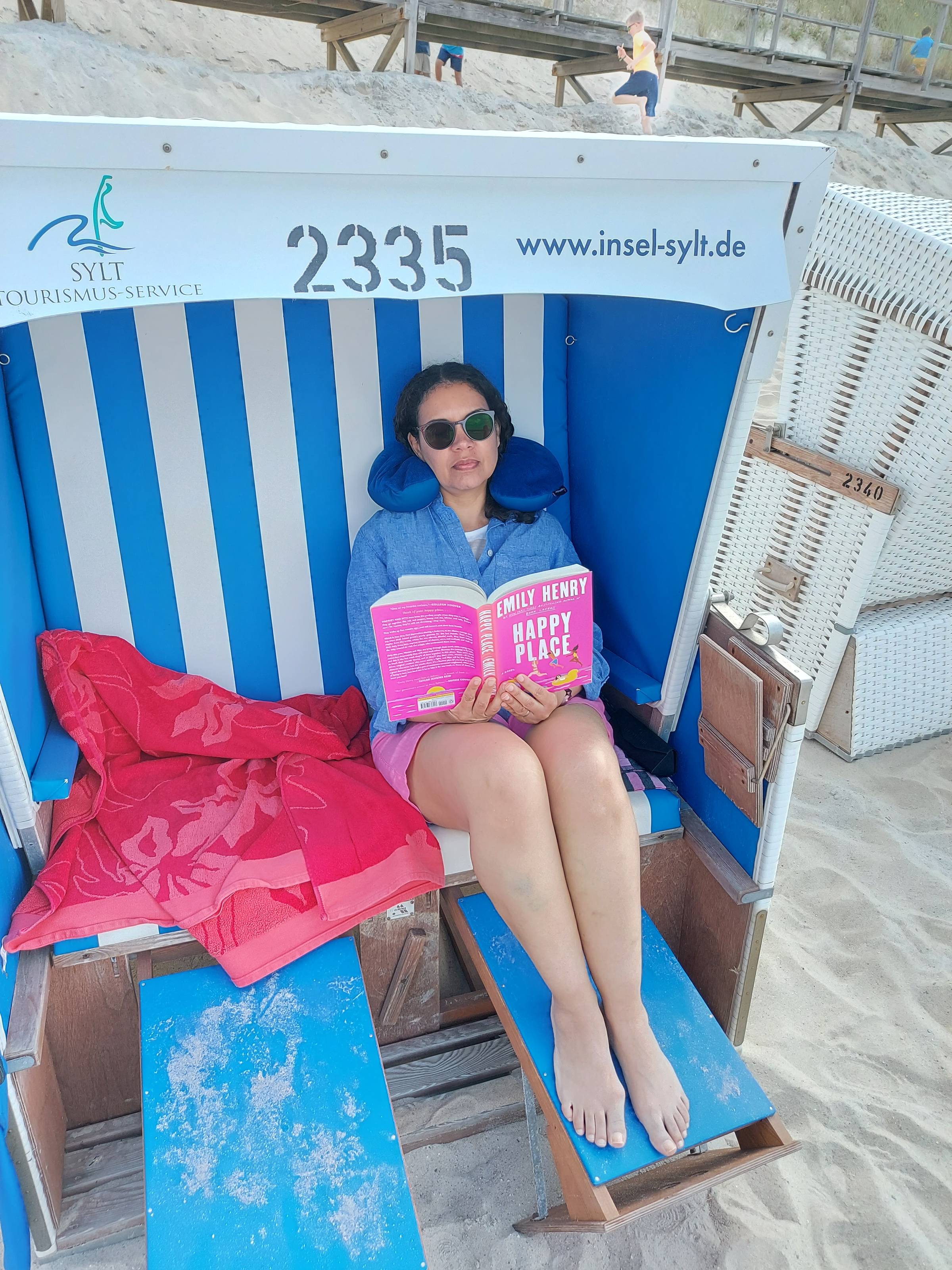 Delise Torres sitting on a beach chair while reading Happy Place by Emily Henry