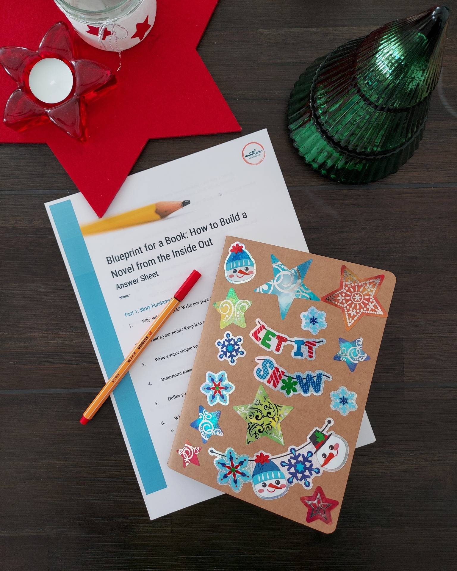 A holiday-themed notebook and a worksheet for Blueprint for a book atop a table and surrounded by Christmas decor