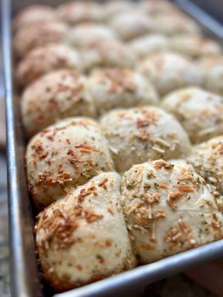 Parmesan herb rolls are nestled together in a pan with golden brown tops.