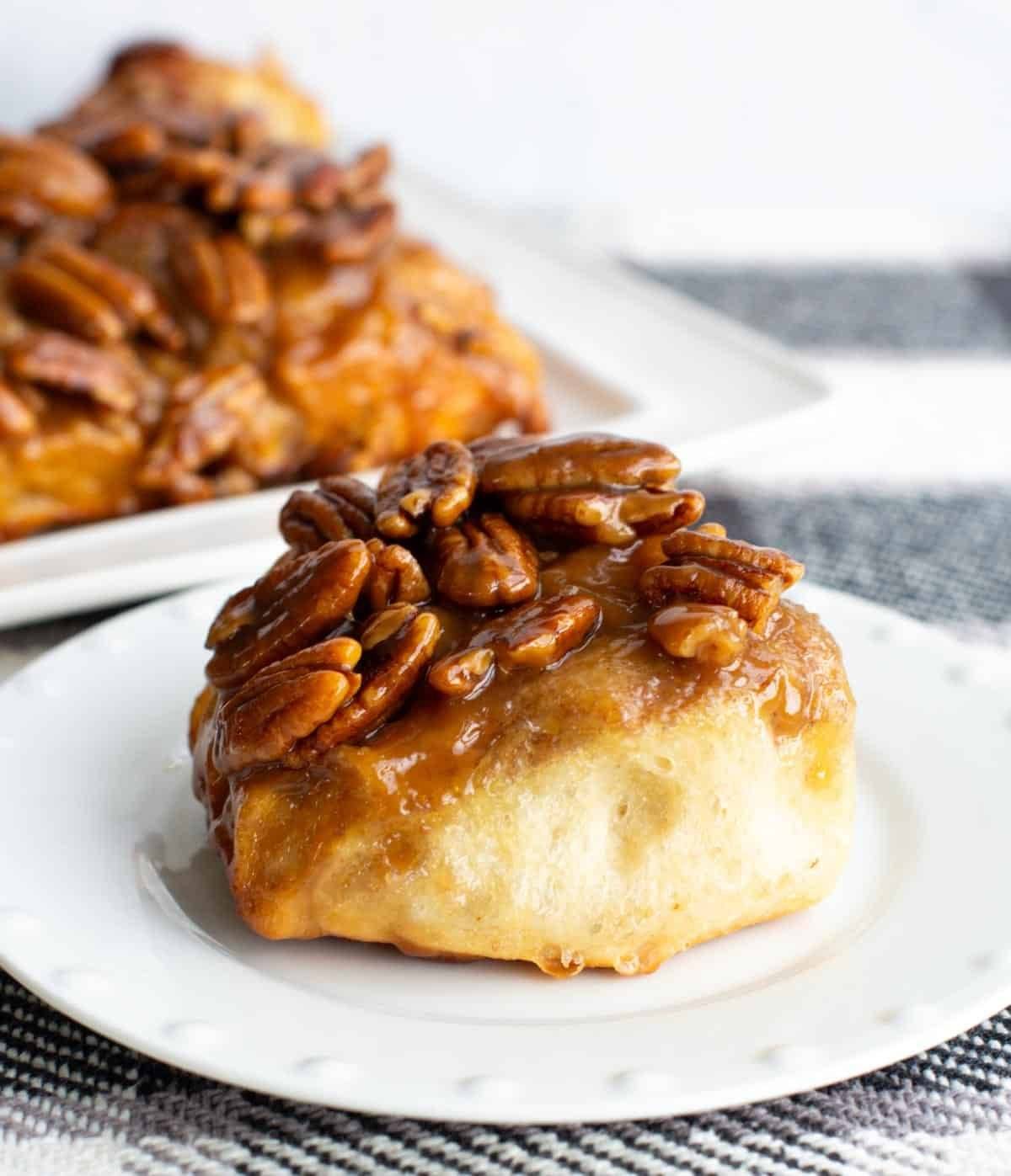 A sticky bun topped with pecans sits on a white plate.