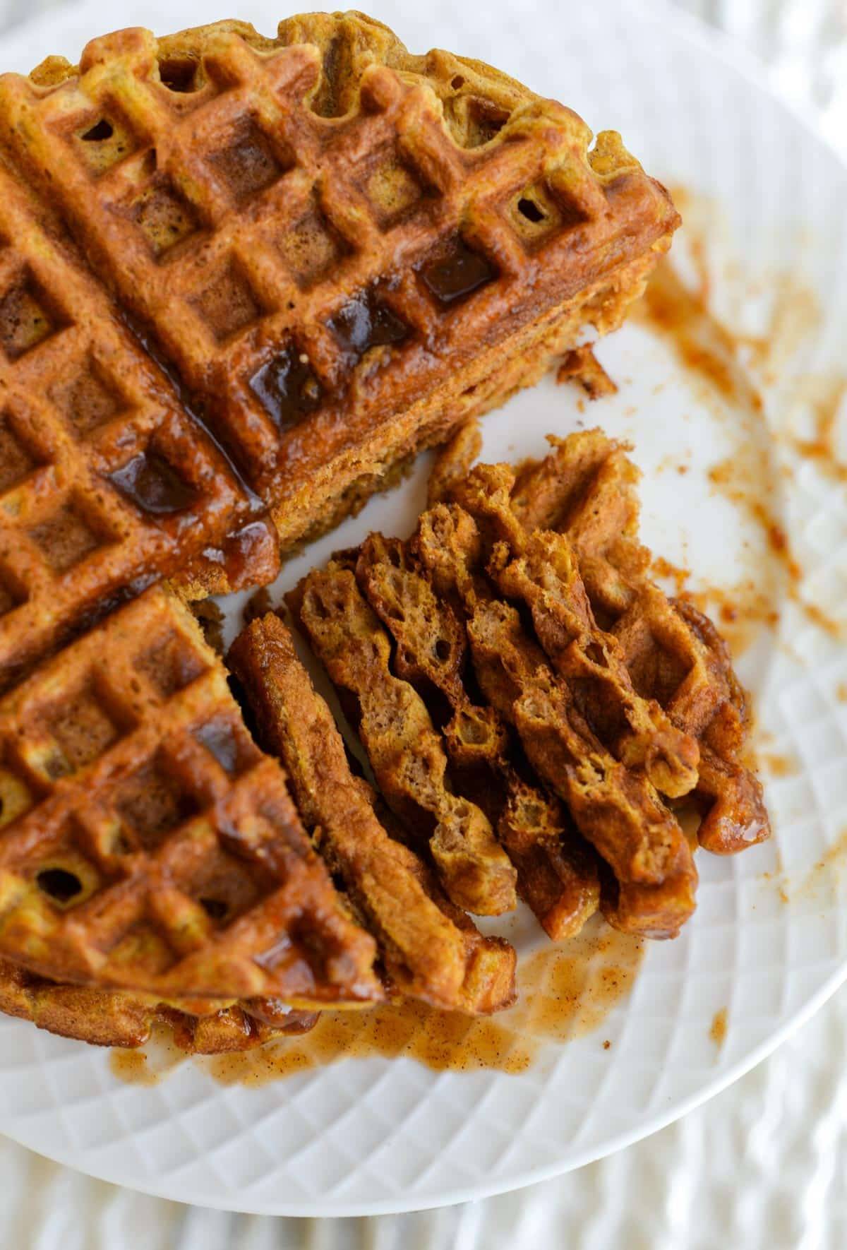 Pumpkin Waffles sit on a white plate covered in syrup.