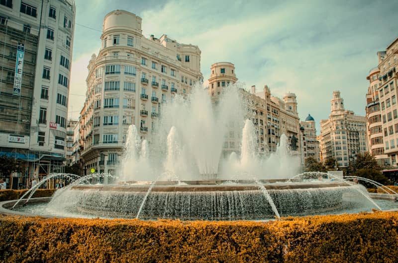 Fountain in a city square with ornate buildings.