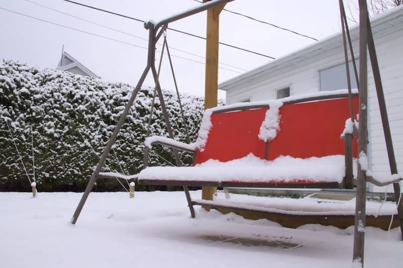 A swing that is covered in snow in front of a house