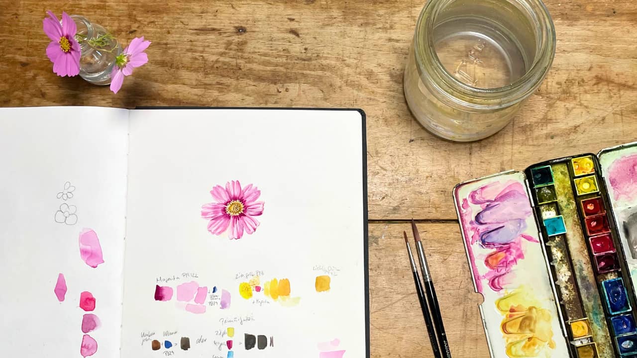 Tischaufsicht mit Skizzenbuch, darin eine gemalte pinke Kosmeenblüte, daneben die Blüte in echt, Pinsel, Aquarellkasten und ein Wasserglas