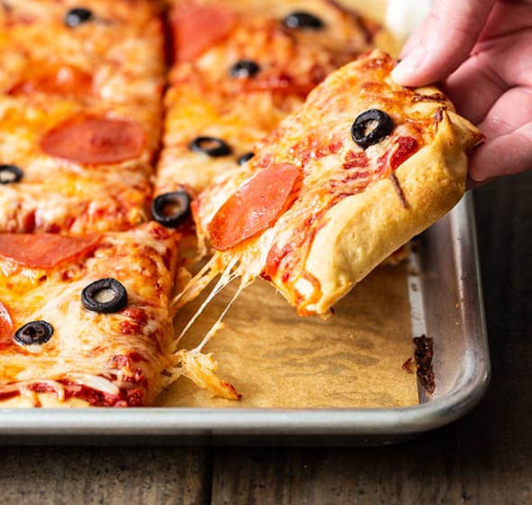 hand holding a piece of gluten free pizza