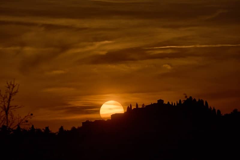 Sunset over a silhouetted mountain and trees.