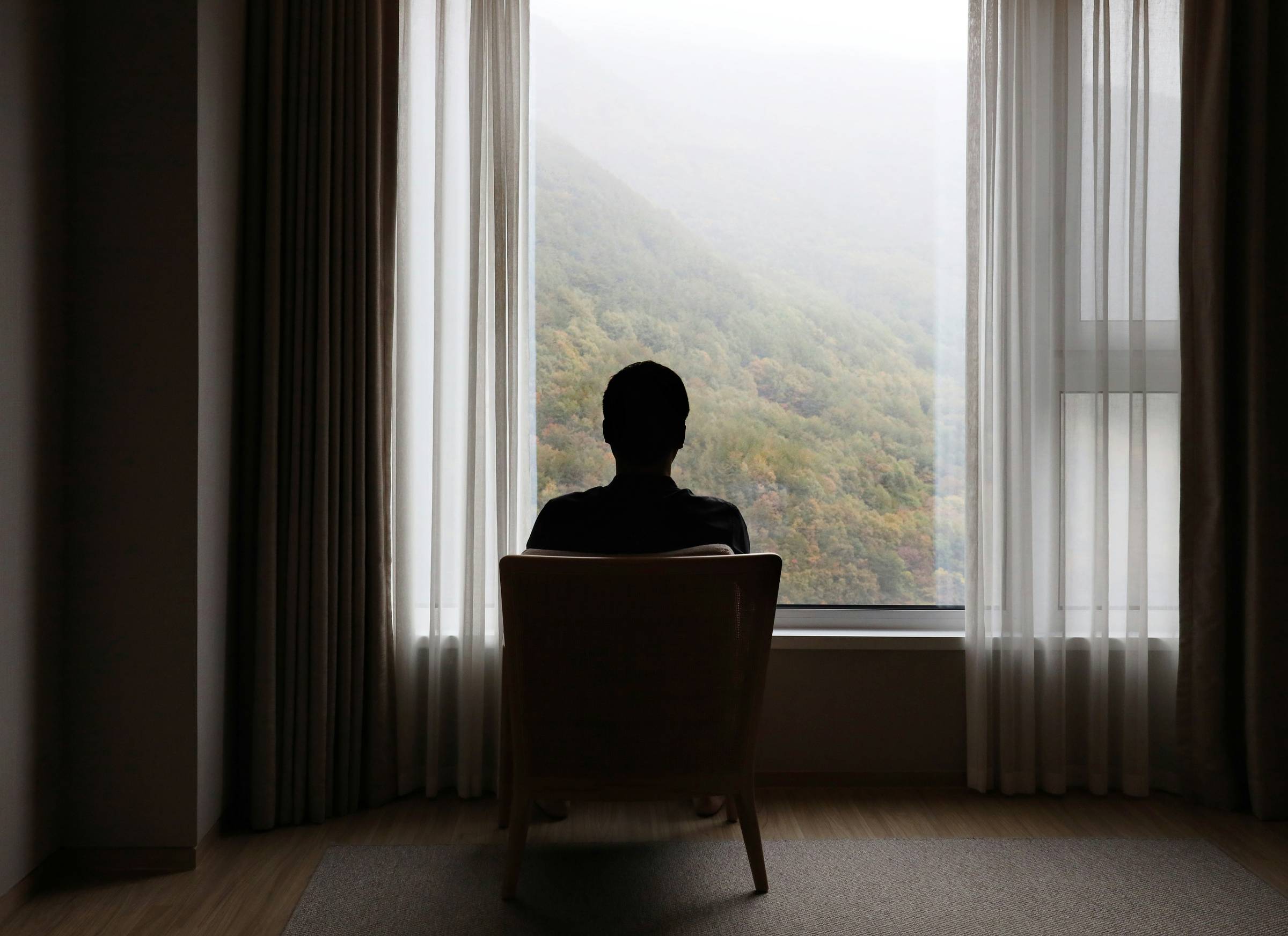 Silhouette of man sitting by a window looking out at mountains