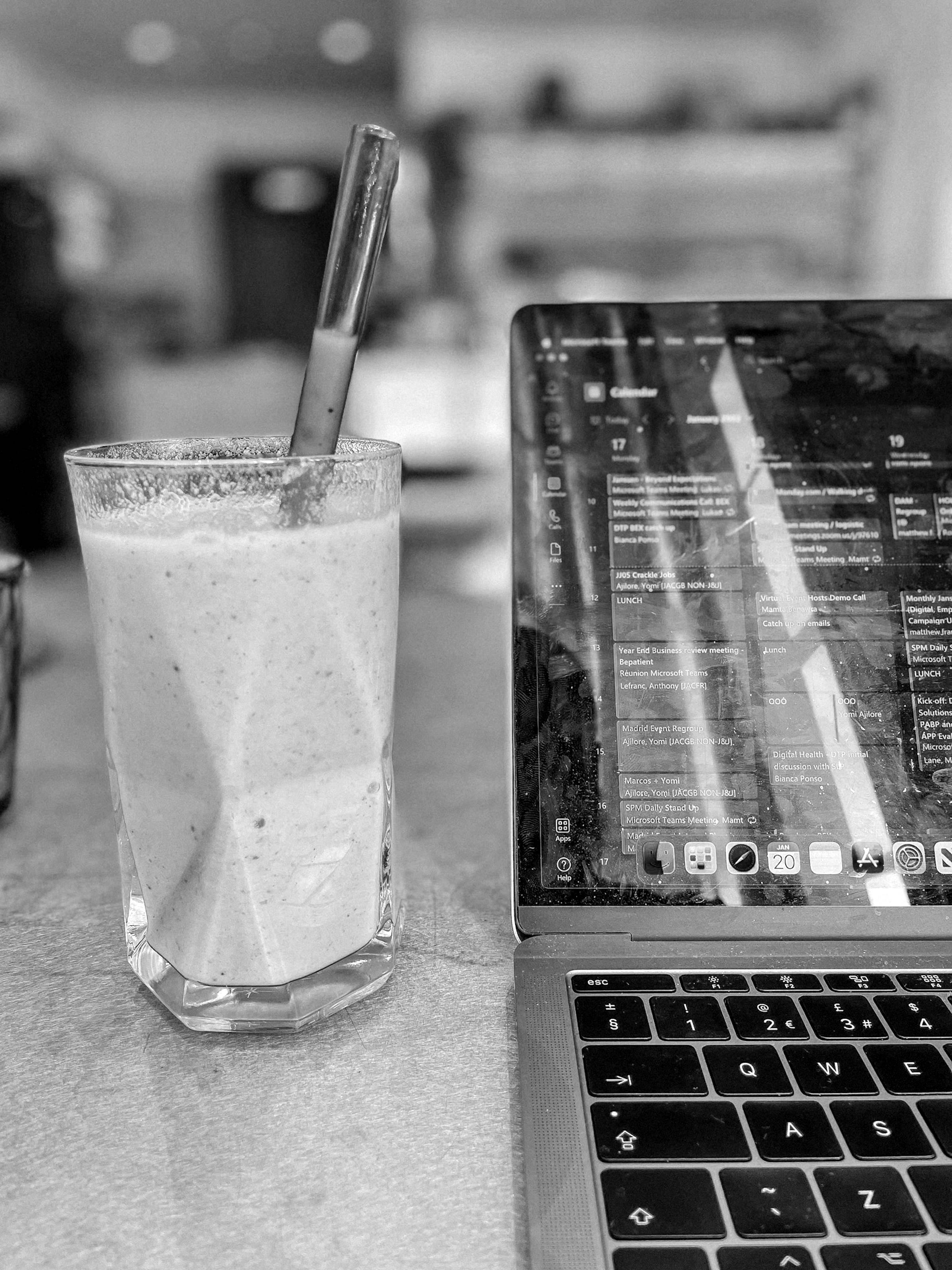 A glass of a smoothie next to a laptop in black and white