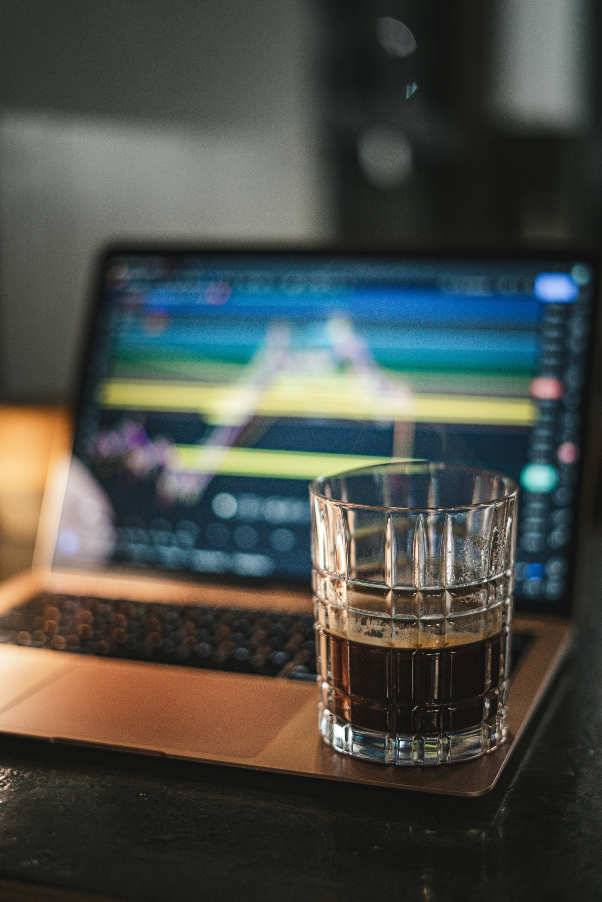 A laptop blurred and a glass with a drink in it sitting on the laptop.