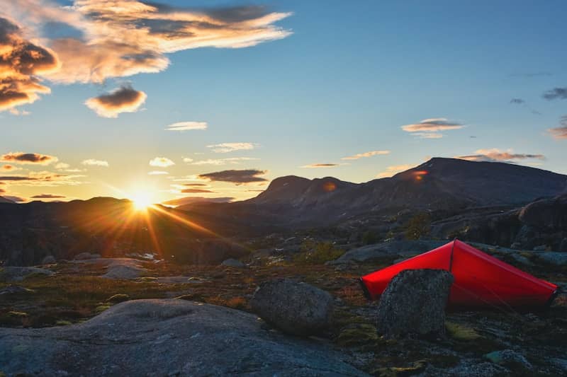Red tent pitched in rocky landscape at sunset