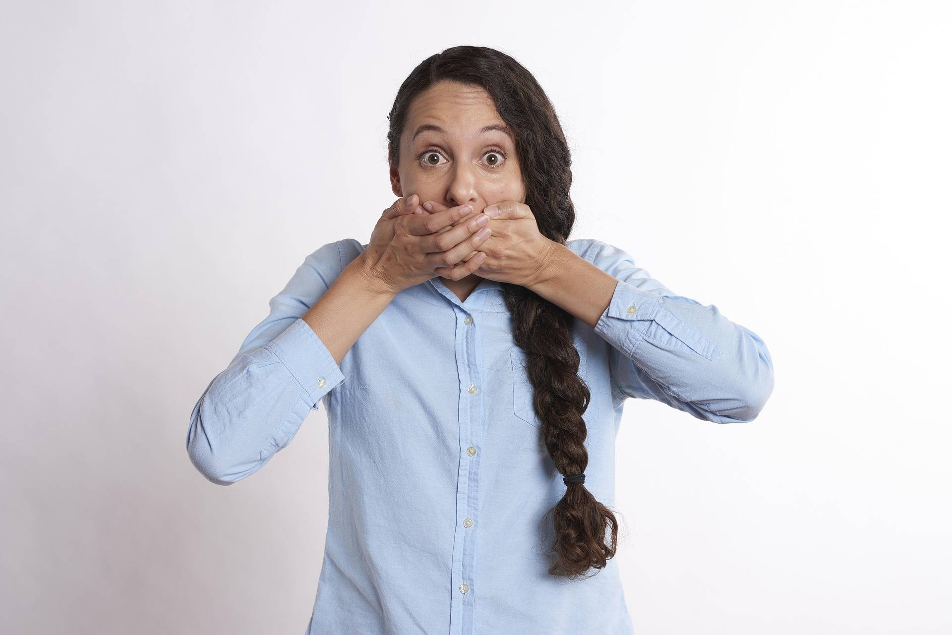 A woman holds her hands over her mouth with a surprised facial expression