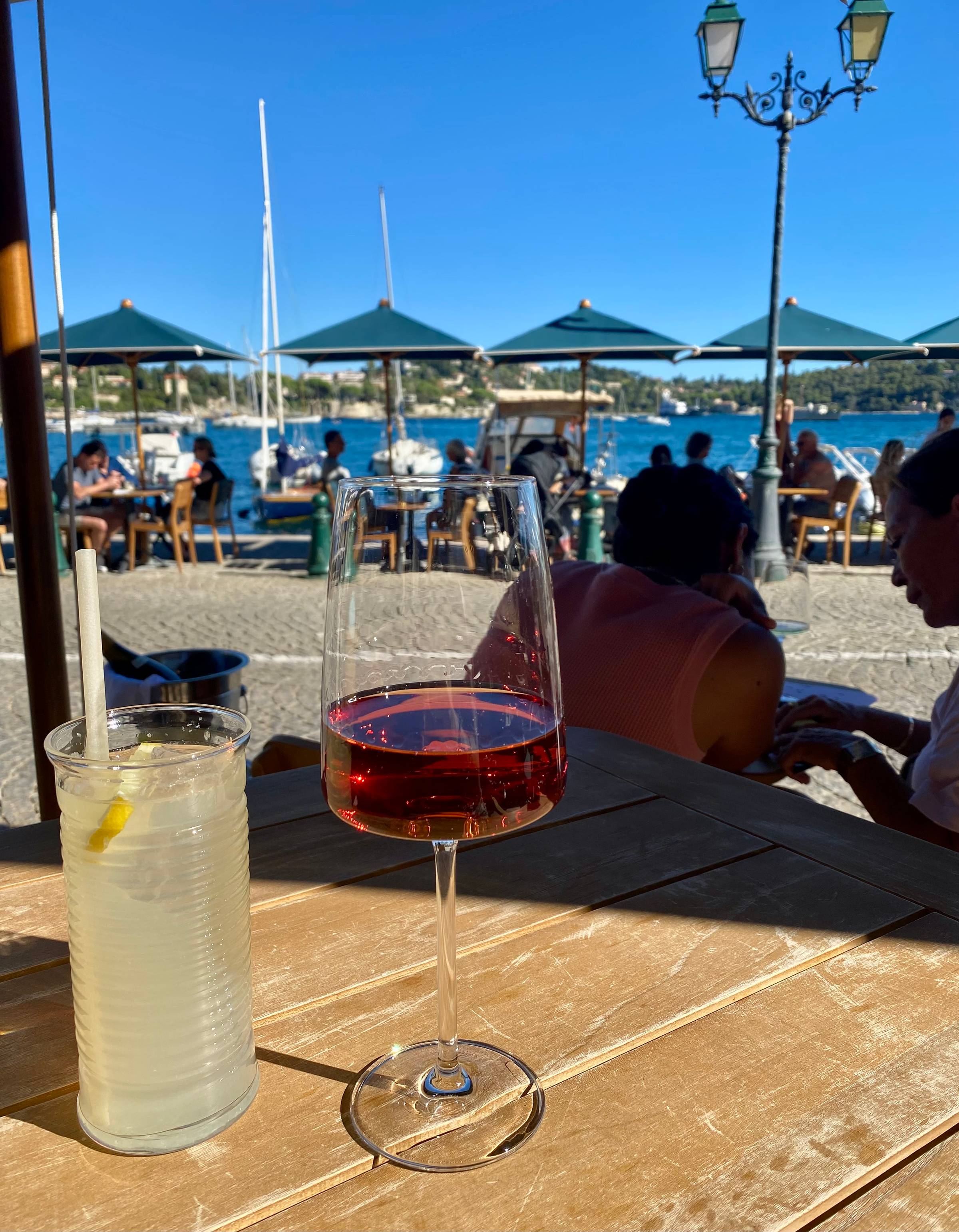A glass of wine and a glass of lemonade on a table in front of the sea