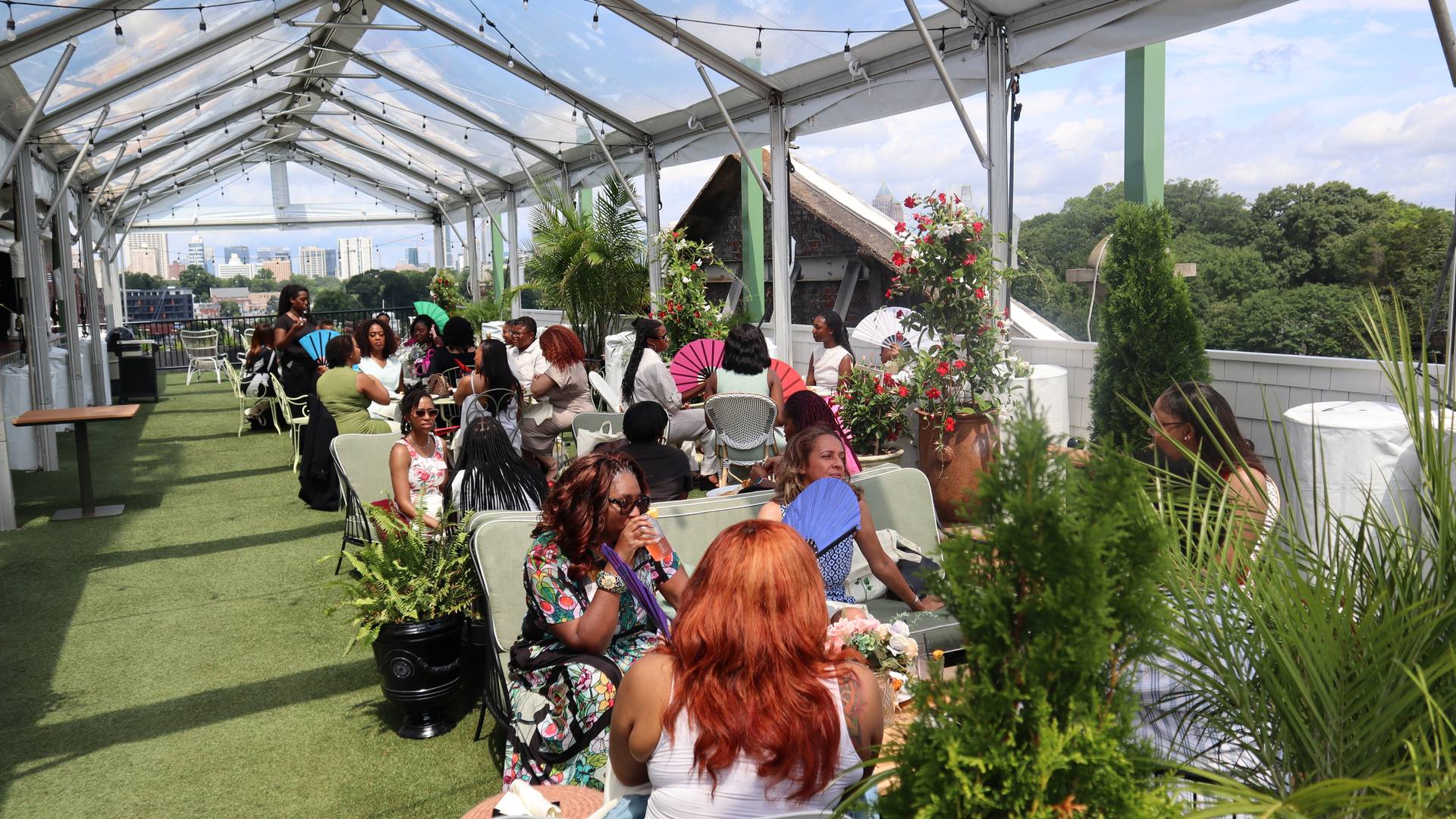 Rooted Brunch guests seated at tables placed along a garden party designed rooftop at Hotel Clermont with the Atlanta skyline in the background