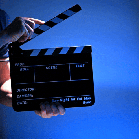 A blue backdrop, a man with a film clapper board enters the frame and clasps the board, and exits the frame. 