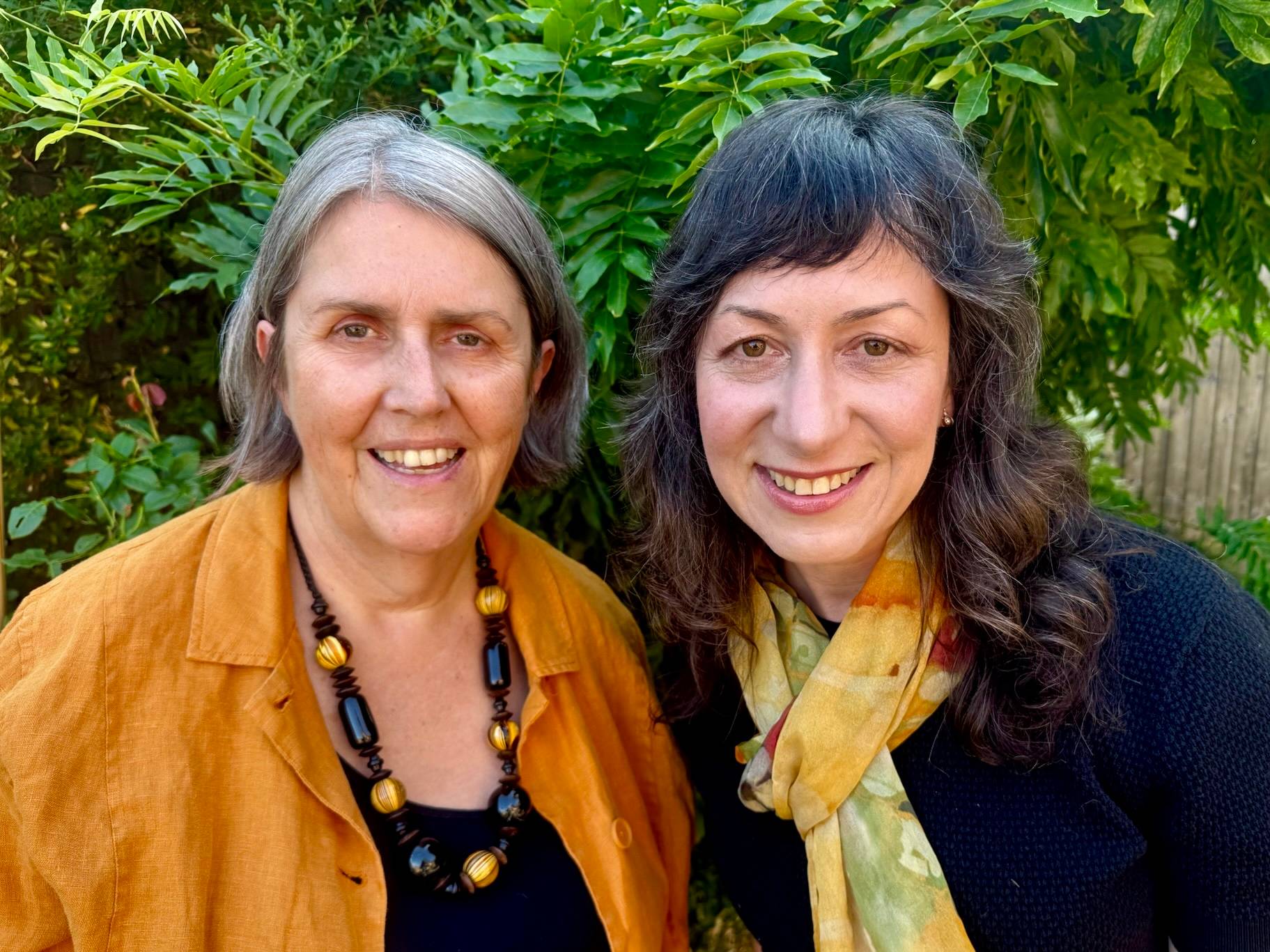 Close-up of Lens Not Label authors Claire and Kim in yellow and black attire. They are standing outside in front of a leafy tree on a sunny day.