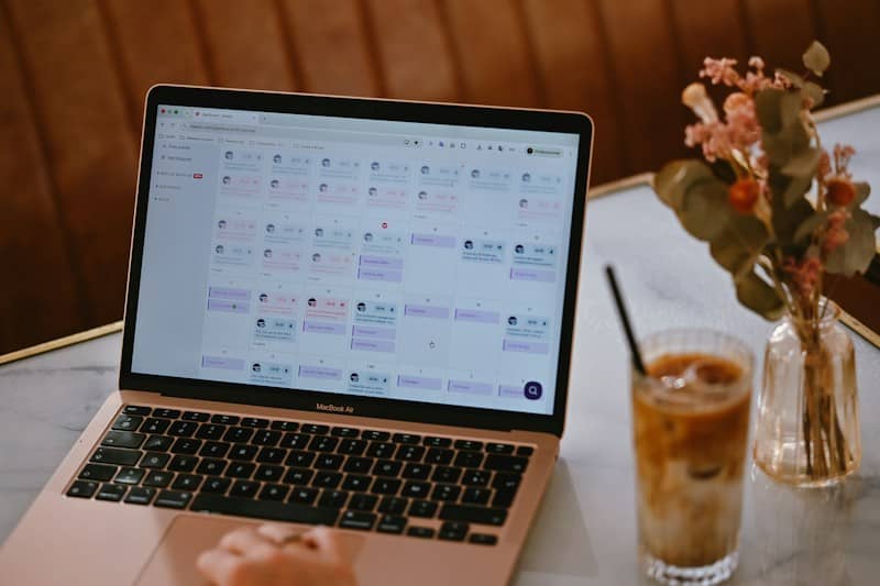 A laptop displaying a social media content calendar beside a glass of iced coffee