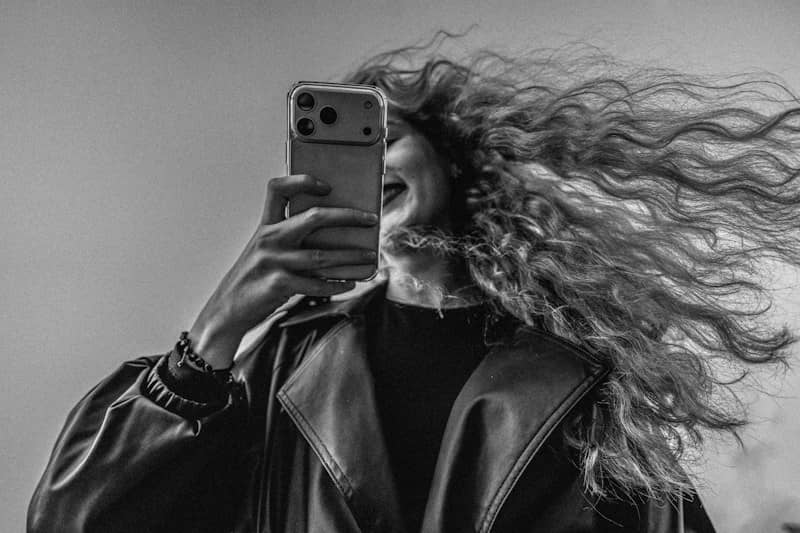 A person with long wavy hair holding a smartphone to their face