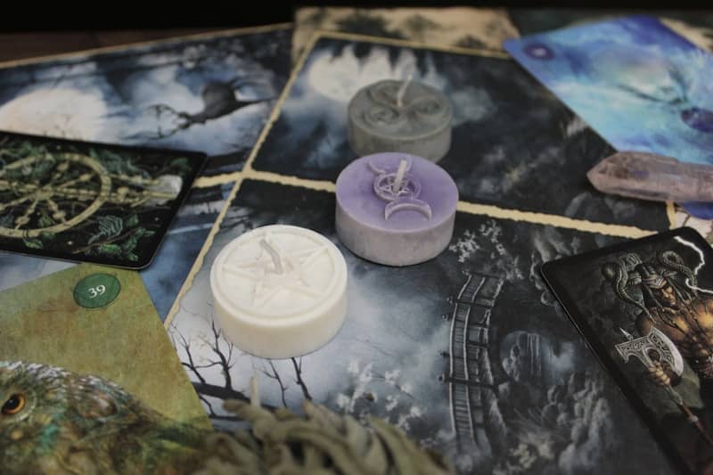 Three small wax candles with embossed symbols on a surface of illustrated tarot cards
