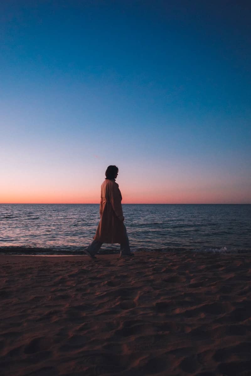 Person strolls along a beach at sunset.