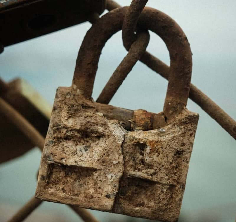 A rusty padlock attached to a chain link fence