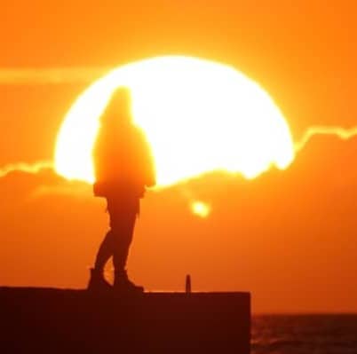 Person silhouetted by the setting sun over the water.