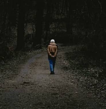 A person walks alone on a dark forest path.