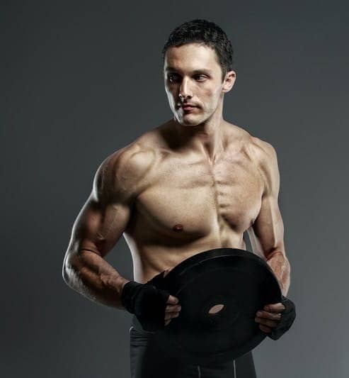 man holding black weight plates standing in front of gray background