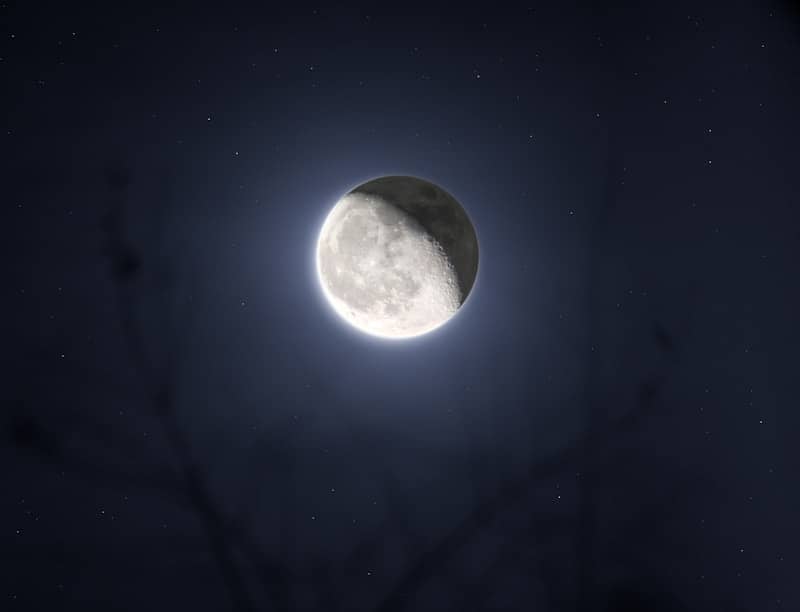 The moon shines brightly in the dark, starry sky.
