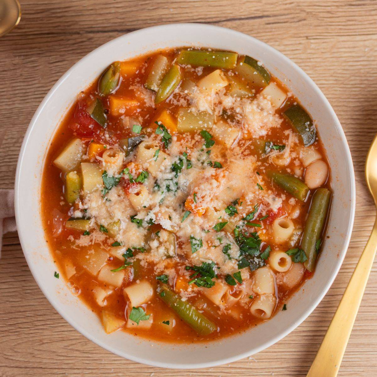 Hearty Italian minestrone soup with vegetables, beans, pasta, and Parmesan cheese in a rustic bowl.