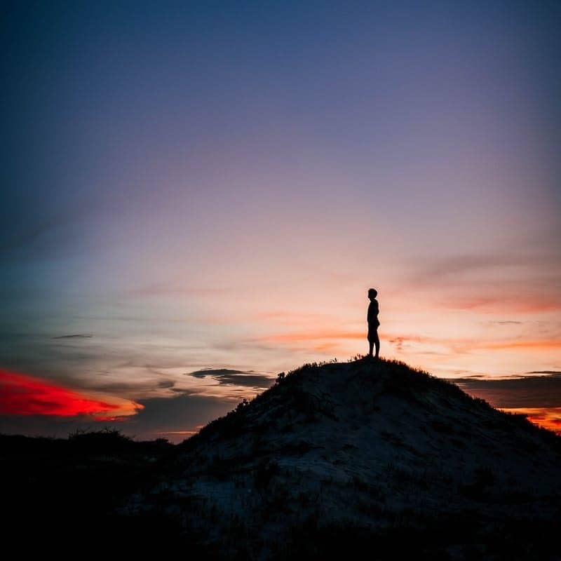 silhouette of person standing on rock formation during sunset