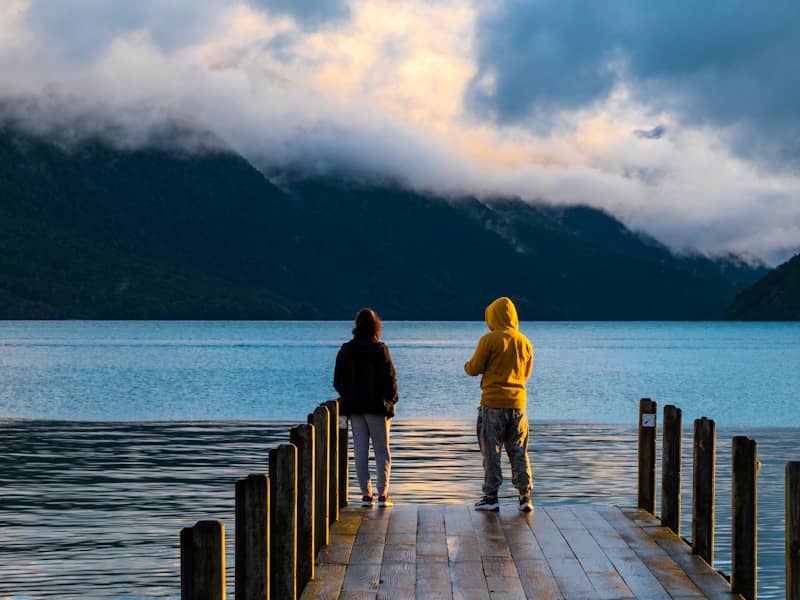 Two people stand on a dock overlooking a lake.