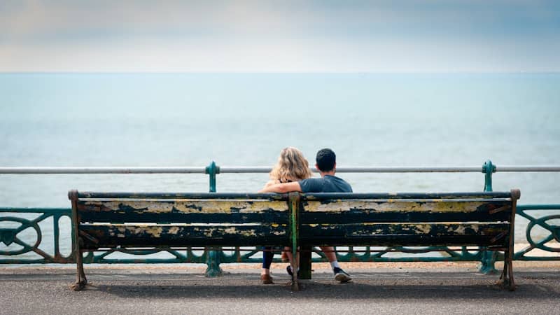 Couple sitting on a bench, looking at the sea.