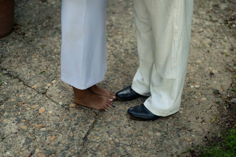 Bare feet of a person beside black shoes on a cracked stone path.