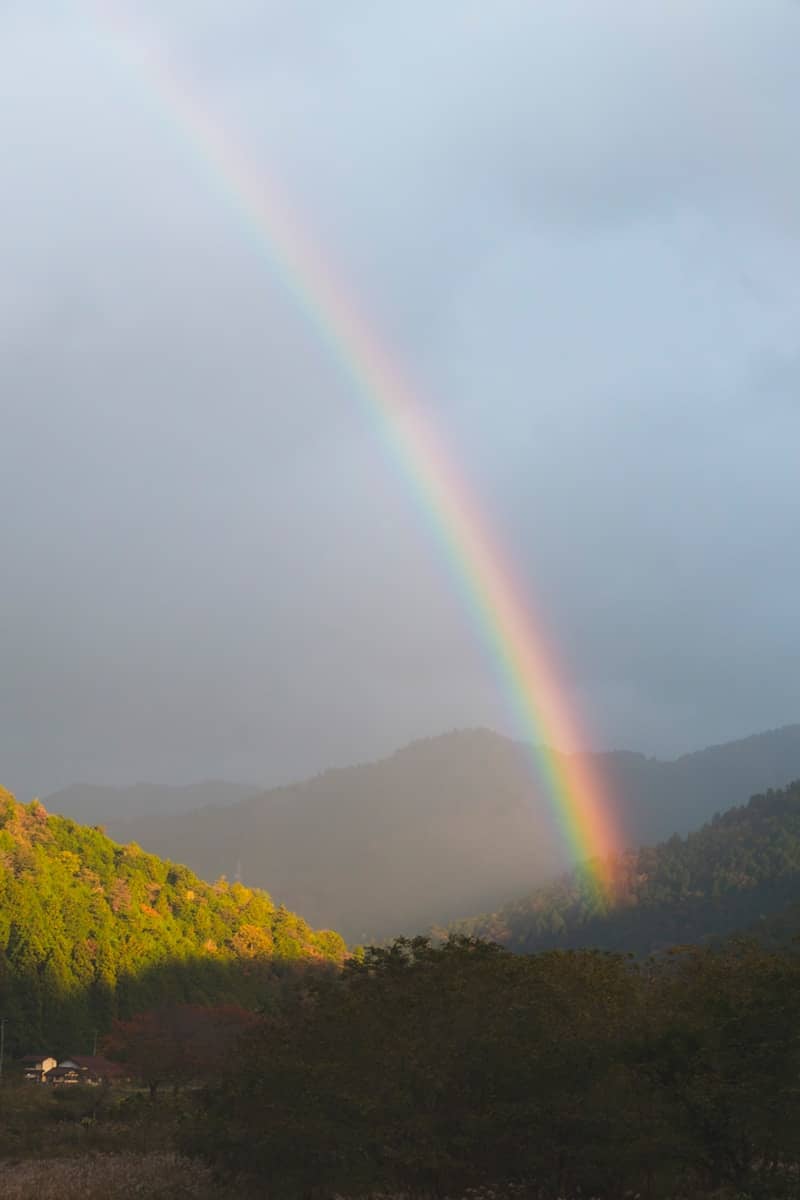 A vibrant rainbow arcs over misty mountains and green hills.