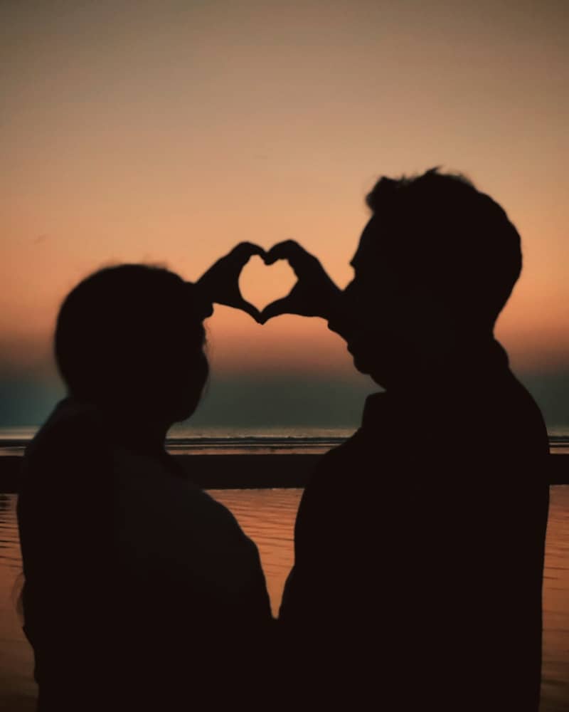 Couple makes a heart shape with hands at sunset.