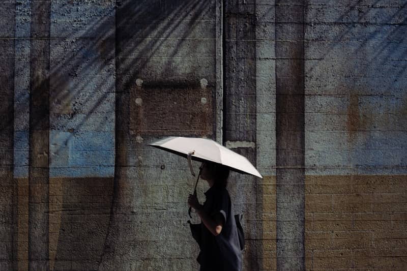 Person with white umbrella walks past a textured wall.