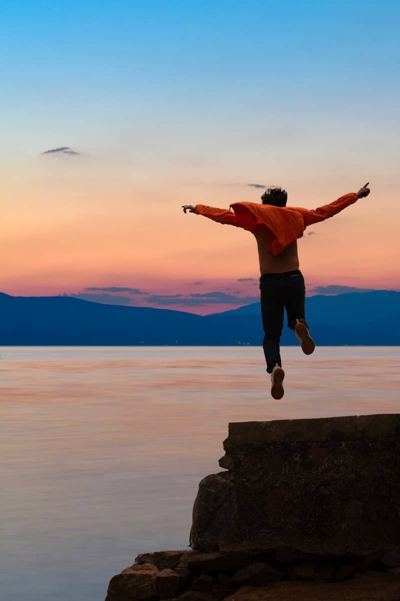 Person jumping off a ledge into the ocean at sunset.