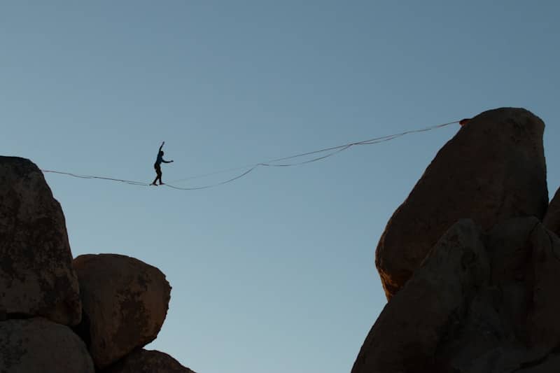 Person balances on tightrope between rock formations