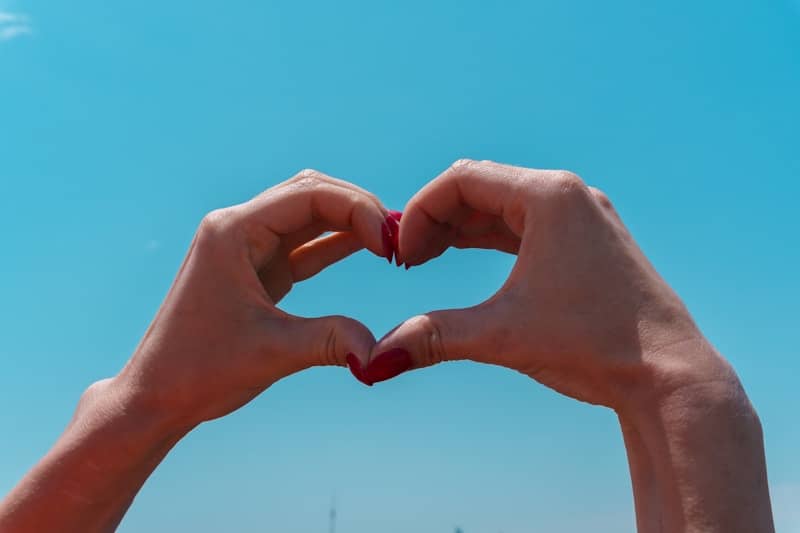 Hands forming a heart shape against blue sky.