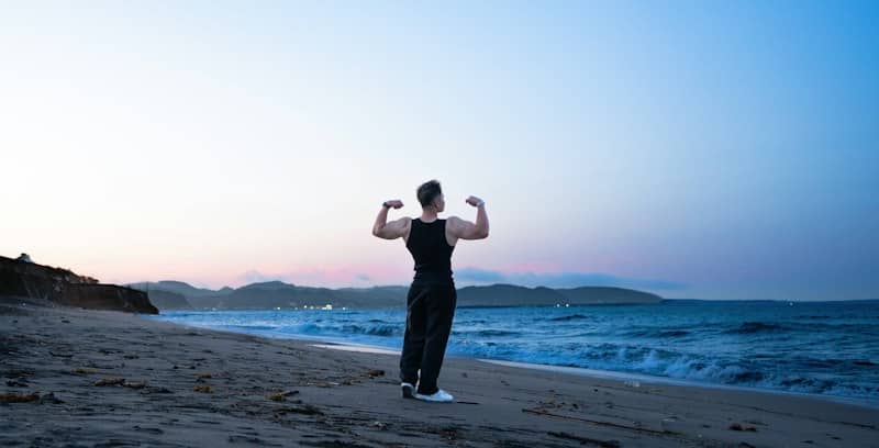 A person flexing muscles on a beach at sunset