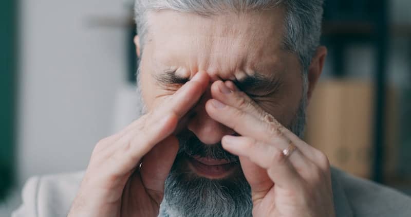 A man with grey hair holding his hands to his face