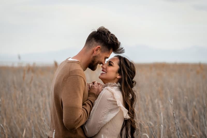Couple looks at each other lovingly in a field.