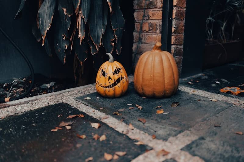 Two pumpkins, one carved for halloween, sit outside.
