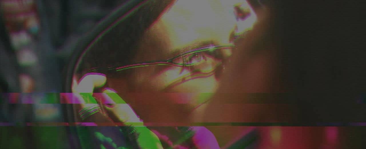 A glitchy close up image of a girl's face. She is wearing thin, metal frame glasses and the predominant colours are green and pink. 